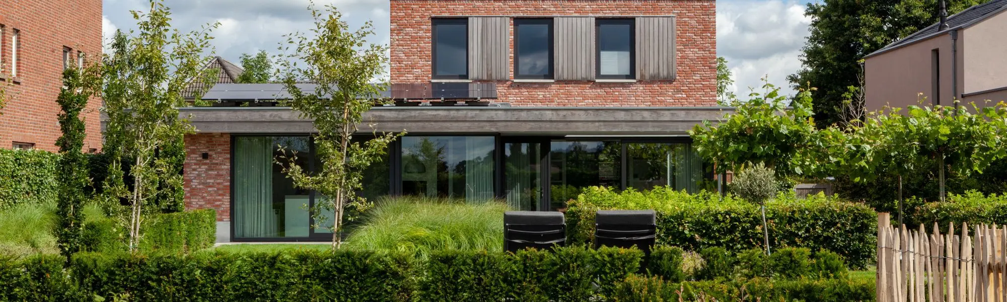 Moderne bakstenen woning met grote glaspartijen en weelderige tuin met hagen en siergrassen