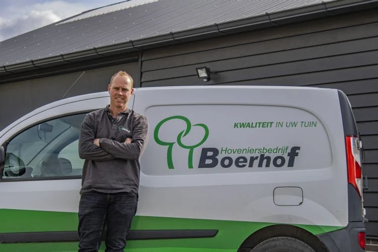 Man staand voor een bedrijfsbus van Hoveniersbedrijf Boerhof met de tekst 'Kwaliteit in uw tuin
