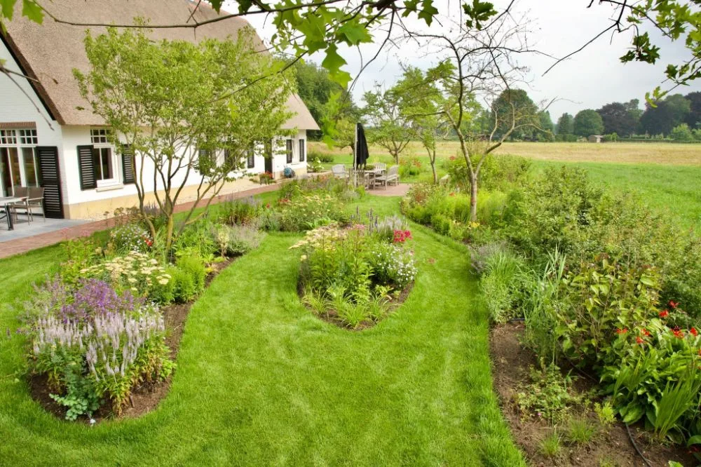 Landelijke tuin met golvende grasbanen, kleurrijke borders en een rieten boerderij op de achtergrond