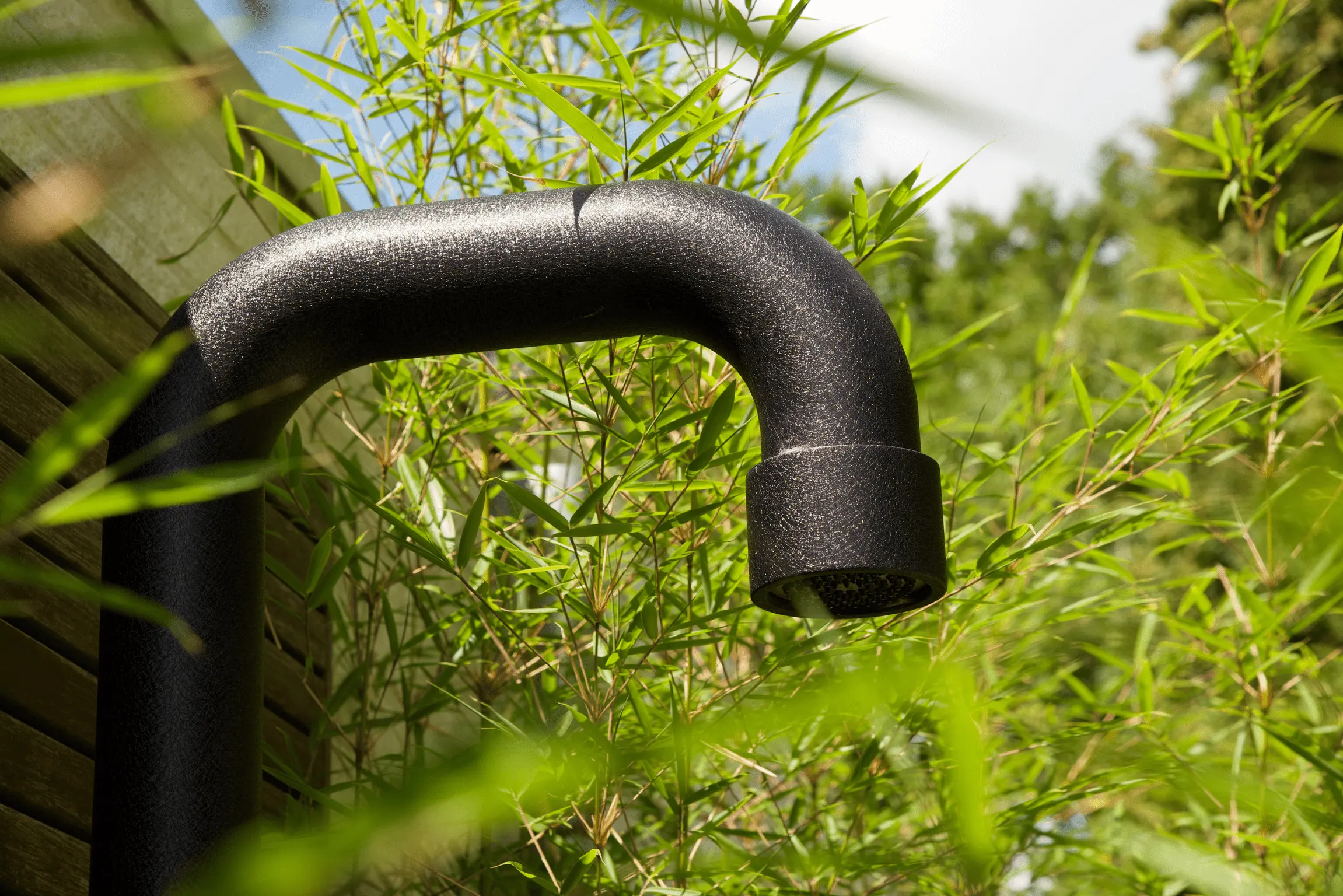 Zwarte douchekop van een buitendouche, omgeven door bamboeplanten in een tuin
